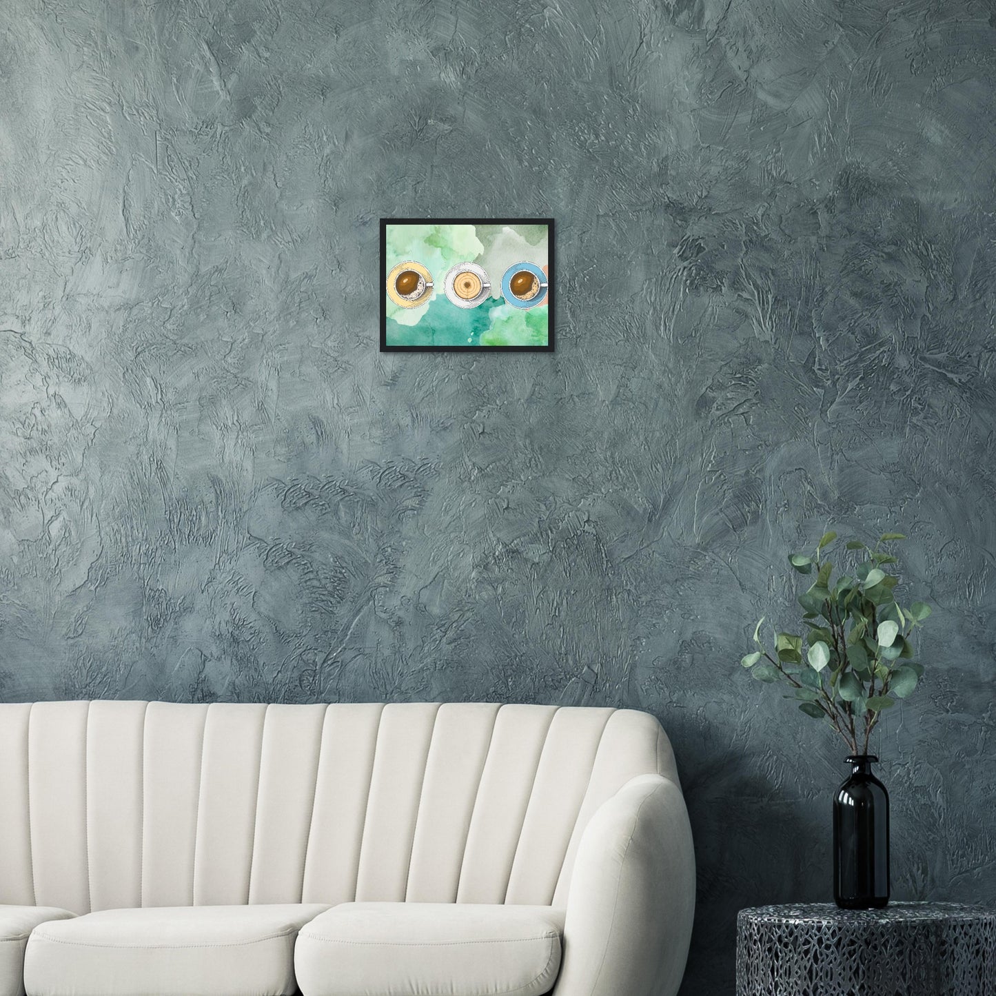 Ein Bild im Schwarzem Rahmen mit buntem Hintergrund in Wasserfarben. Im Vordergrund Sind Drei Tassen Kaffe. Eine Tasse Beige, Weiß und Blau. Das Bild hängt über einem Sofa an einer dunklen Wand im Wohnzimmer..