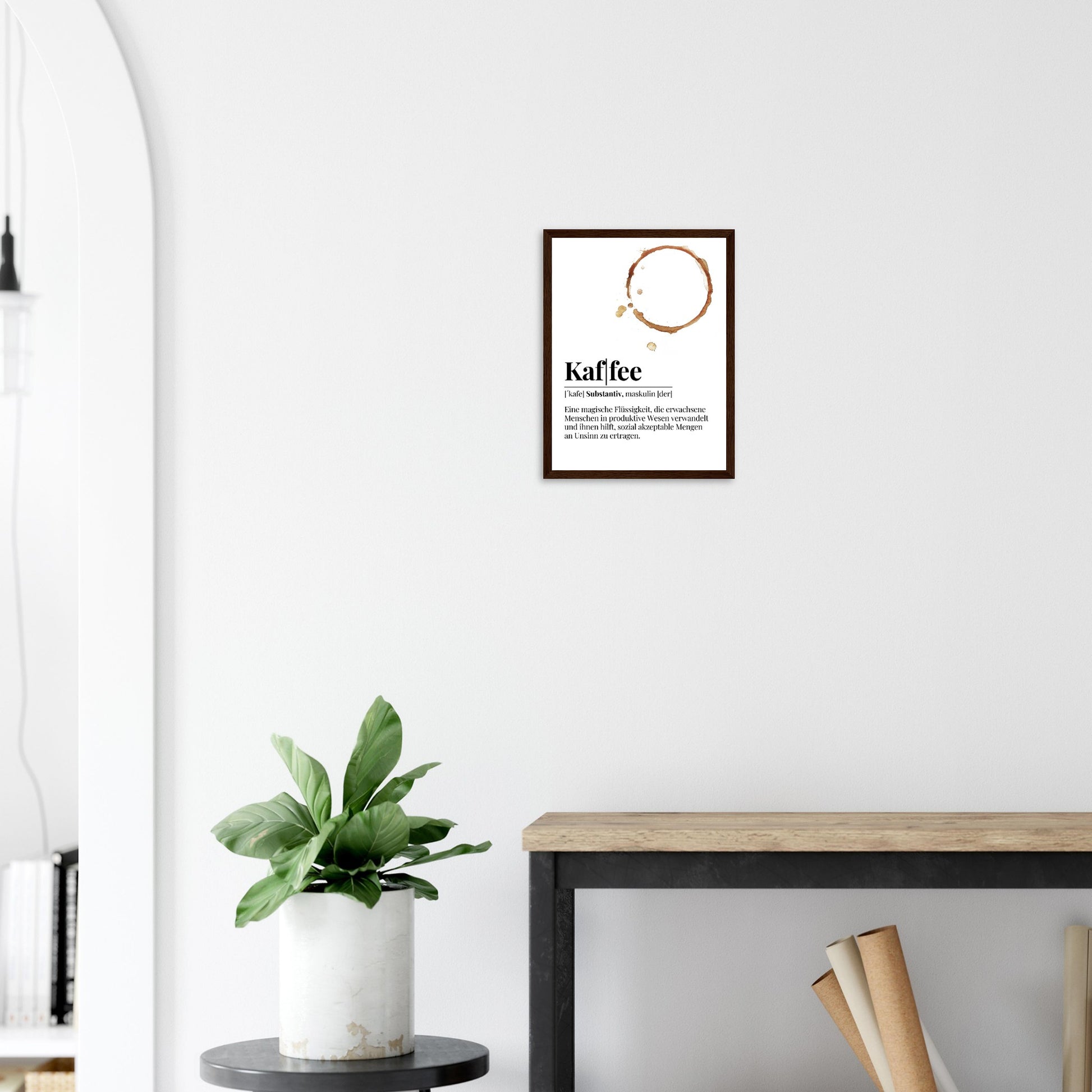 Ein Bild im Holzrahmen mit der Definition von Kaffee mit einem frechen Spruch als Definition. Mittig im Bild befindet sich ein Kaffee Tassenabdruck. Das Bild hängt über einem Tisch an der Wand.