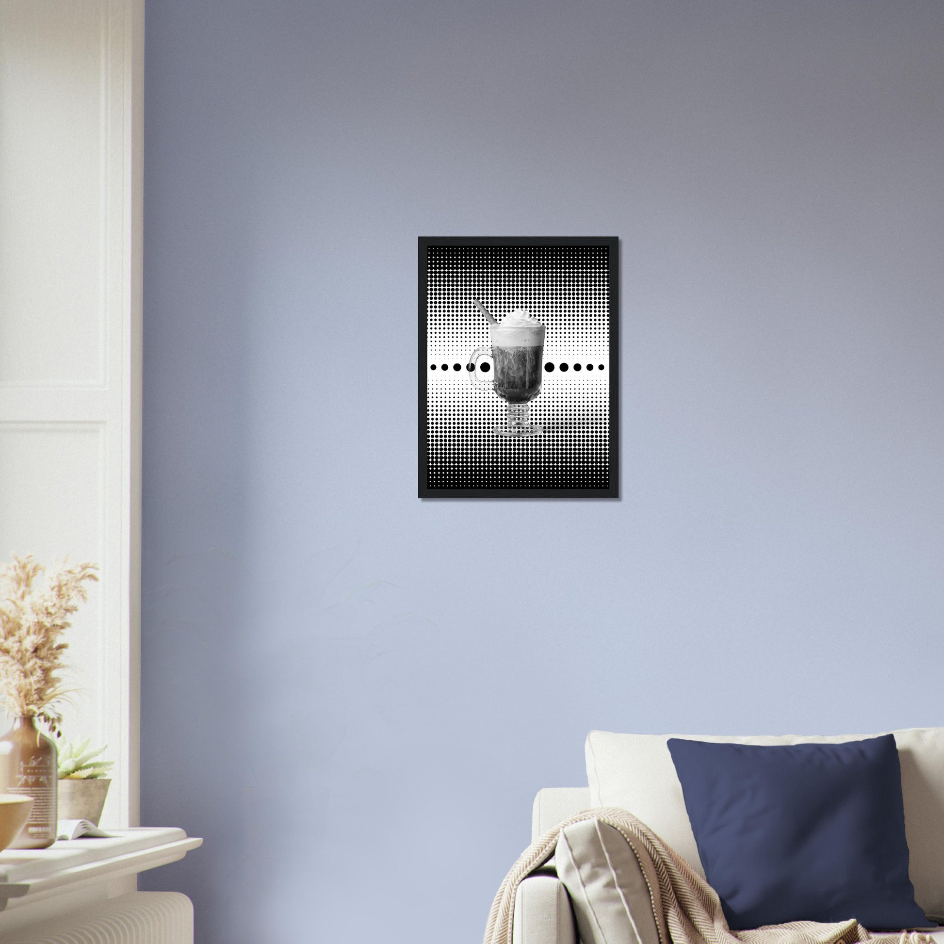 Bild im schwarzem Rahmen mit einem Schwarz weißem Motiv aus schwarzen punkten auf einem weißen Untergrund gepaart eines Schwarzweiß Foto eines Cappuccino an einer Blauen Wohnzimmer wand.